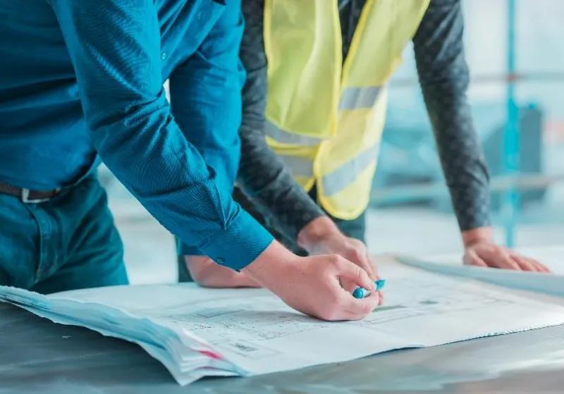 Deux personnes examinent des plans, l'une d'elles porte un gilet de sécurité jaune.